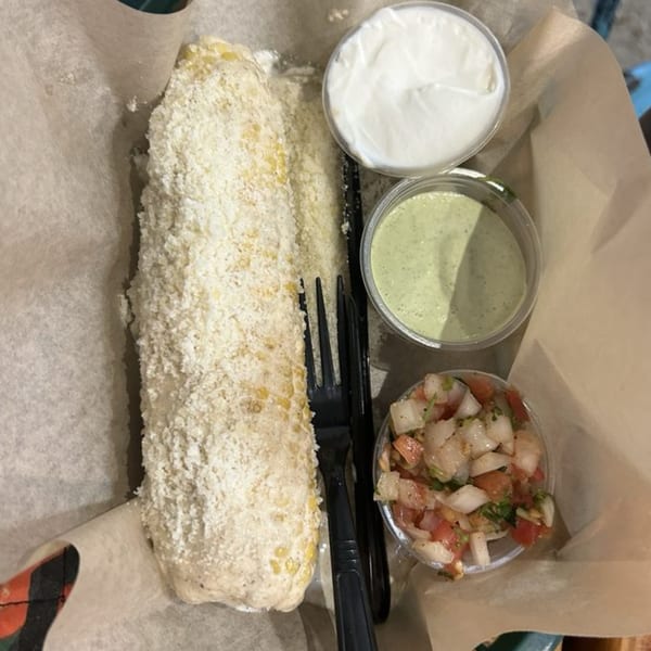 Elote, sour cream, green sauce, and pico de gallo in a paper-lined basket from Taco Station.