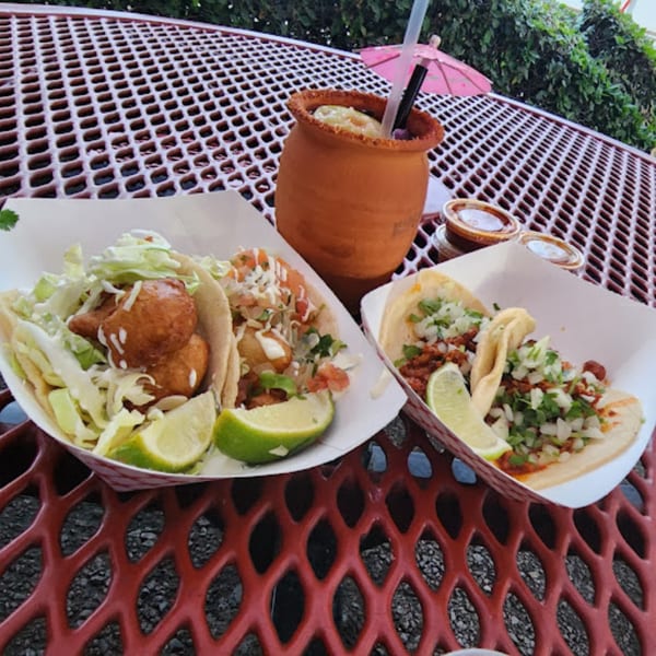 Two baskets of tacos, one with fish tacos and the other with carne asada, on a red patio table.