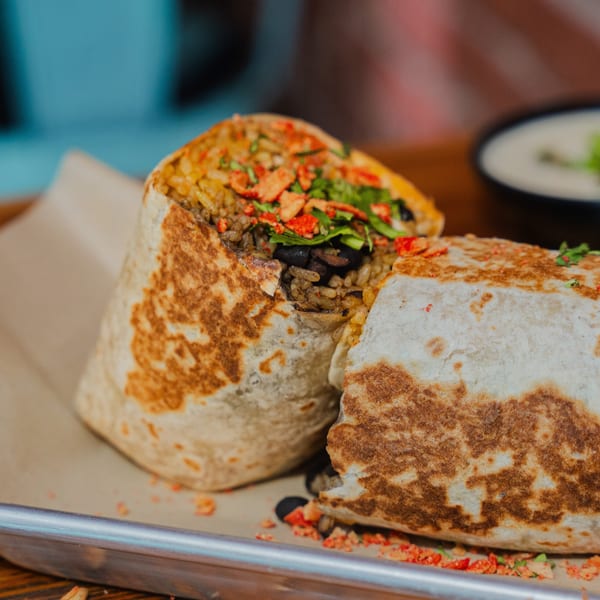 A large, cut burrito from Taco Station, revealing rice, black beans, and colorful toppings.