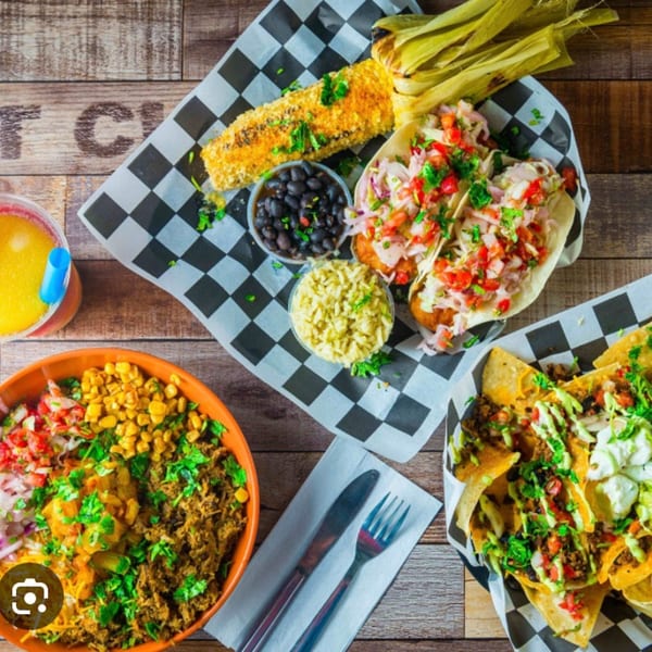 Overhead view of Taco Station's Mexican dishes: tacos, nachos, corn, rice, beans, and a drink.