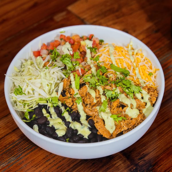 A vibrant Taco Station burrito bowl with chicken, black beans, shredded cabbage, pico de gallo, cheese, and green sauce.