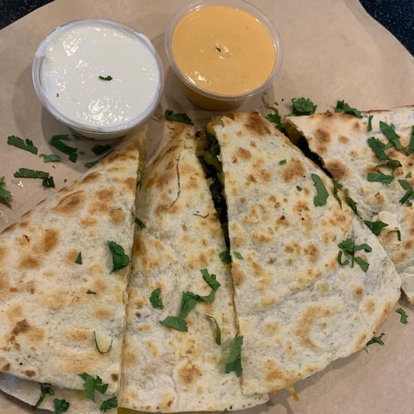 Four quesadilla slices with cilantro, served with white sour cream and orange cheese sauce.