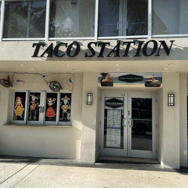 Exterior of Taco Station with a large sign, glass doors, and decorative skeleton figures in the windows.