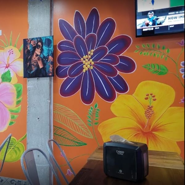 Vibrant orange wall with large painted flowers, a framed Day of the Dead art piece, and a TV.